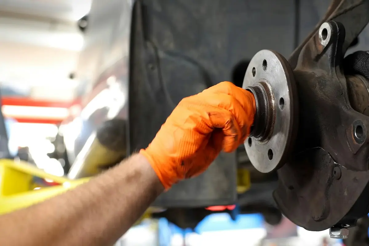 Mano con guante revisando el buje y la mangueta de la rueda de un coche elevado en un taller