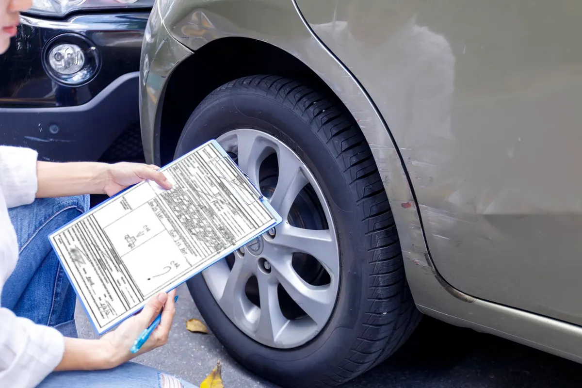 Persona rellenando un formulario junto a la rueda de un coche